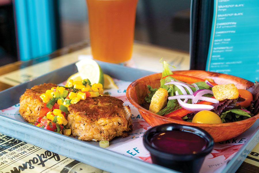 A spread of fish and crab cake variations served up on a silver platter with side dishes of roasted tricolored potatoes and a spring mix salad. Photography by Wyatt Kostygan